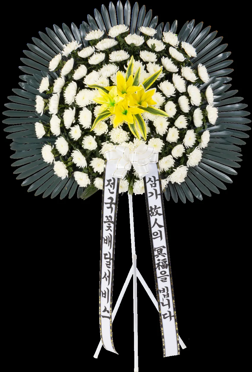 Round sympathy wreath of white chrysanthemums with a yellow lily centre and dark palm-leaf halo, two white sashes, on a white tripod stand