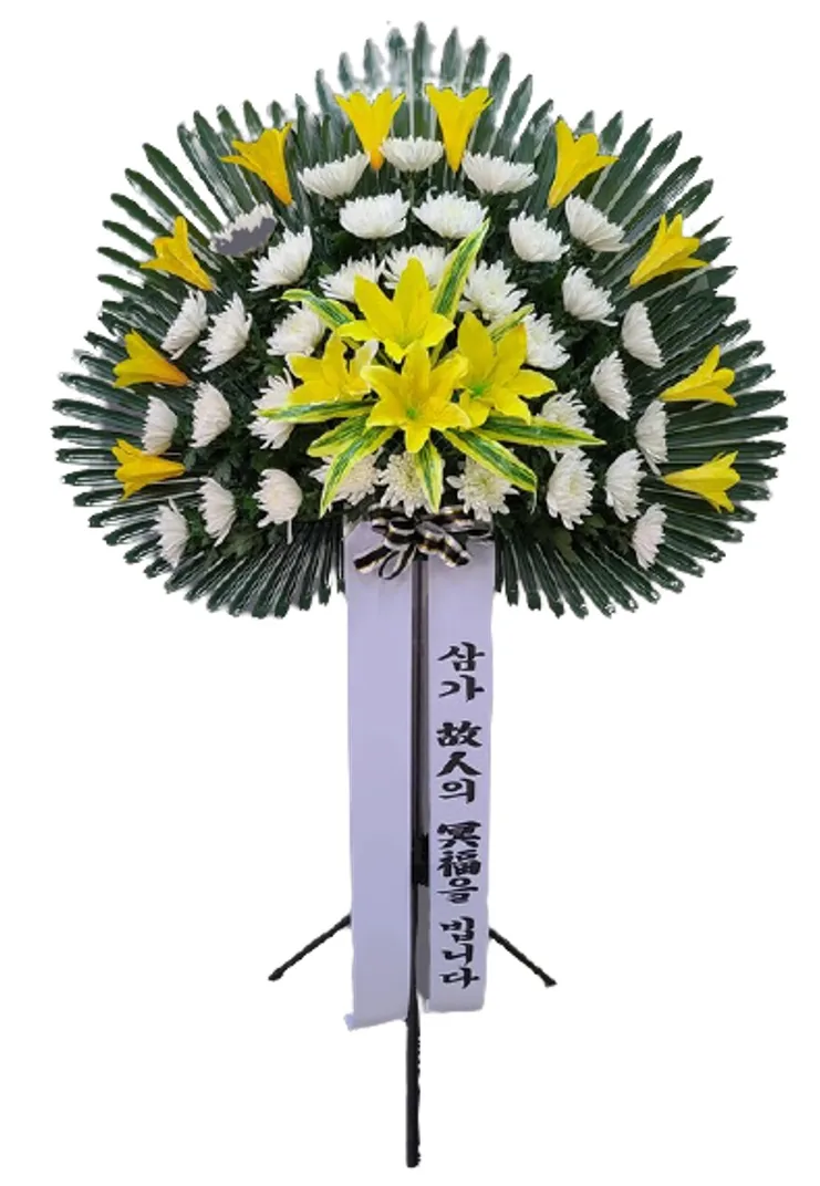 Standing sympathy arrangement of white chrysanthemums, yellow lilies and yellow accent flowers on a fan of dark green foliage, with a white condolence sash on a metal stand
