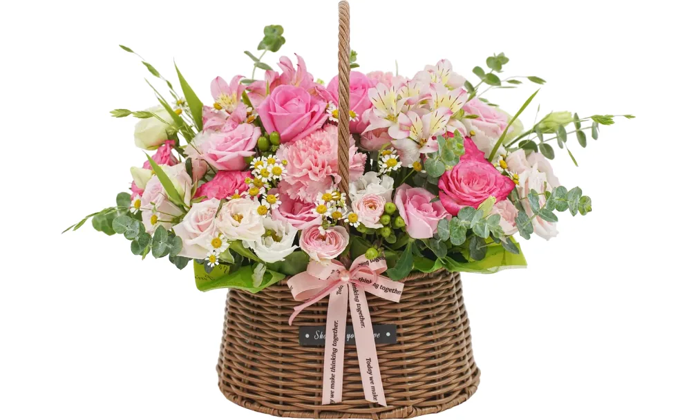 Hot pink and soft pink roses, a pink carnation, pink alstroemeria, tiny white daisies and green berries in a brown wicker basket with a pink printed ribbon
