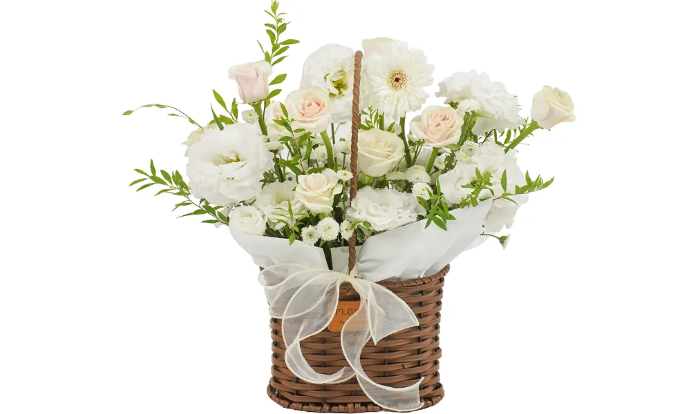 Giỏ mây sẫm màu có quai với đồng tiền trắng, cát tường trắng, hoa hồng kem và phớt hồng cùng cúc nút nhỏ trắng, lá xanh và ruy băng ngà mỏng