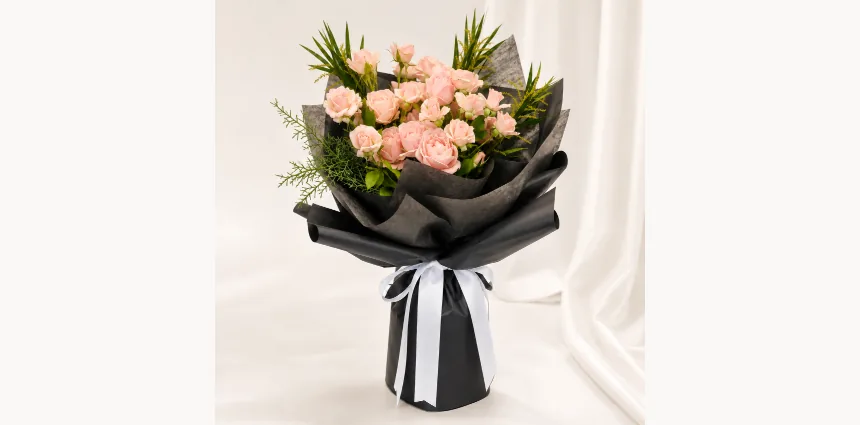 Pink Noir bouquet of pale pink spray roses in matte black wrapping with a black-and-white ribbon, studio shot on silk fabric